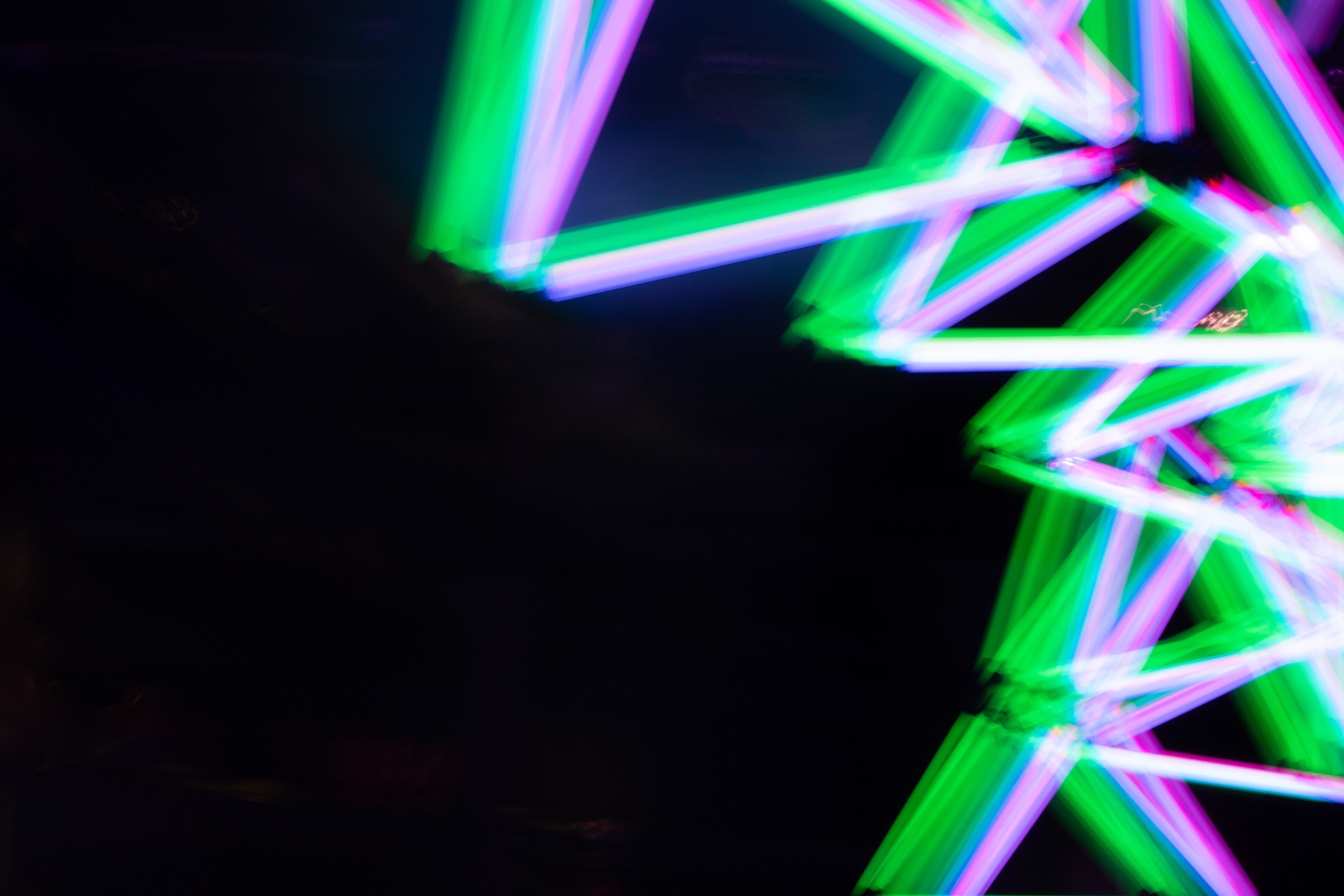 Blurred neon lights forming abstract geometric shapes in green, blue, and pink on a black background.
