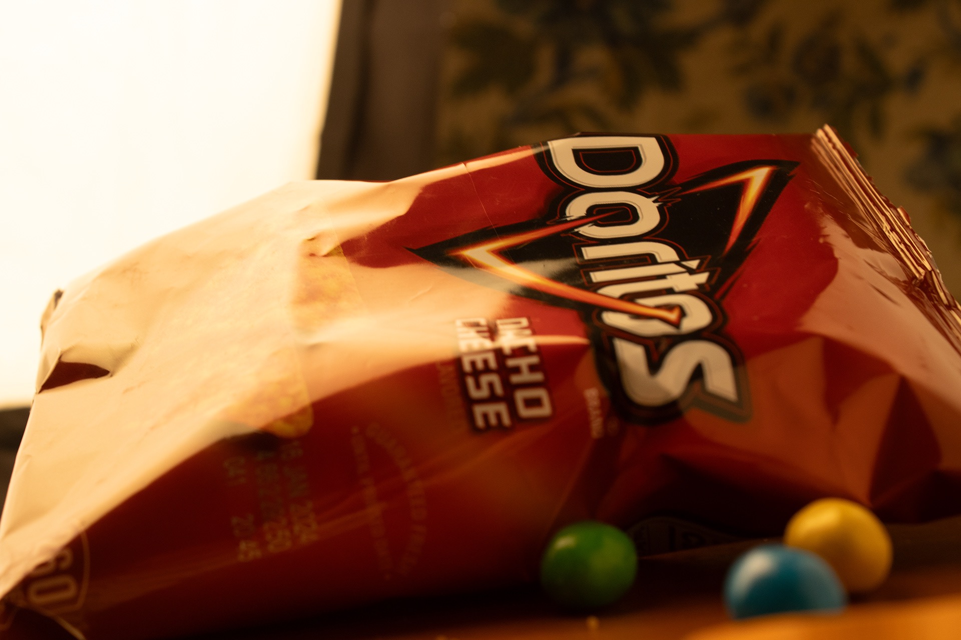 A bag of Doritos Flame Roasted Fiery Habanero chips lying on its side next to three colorful candy pieces in green, blue, and yellow.