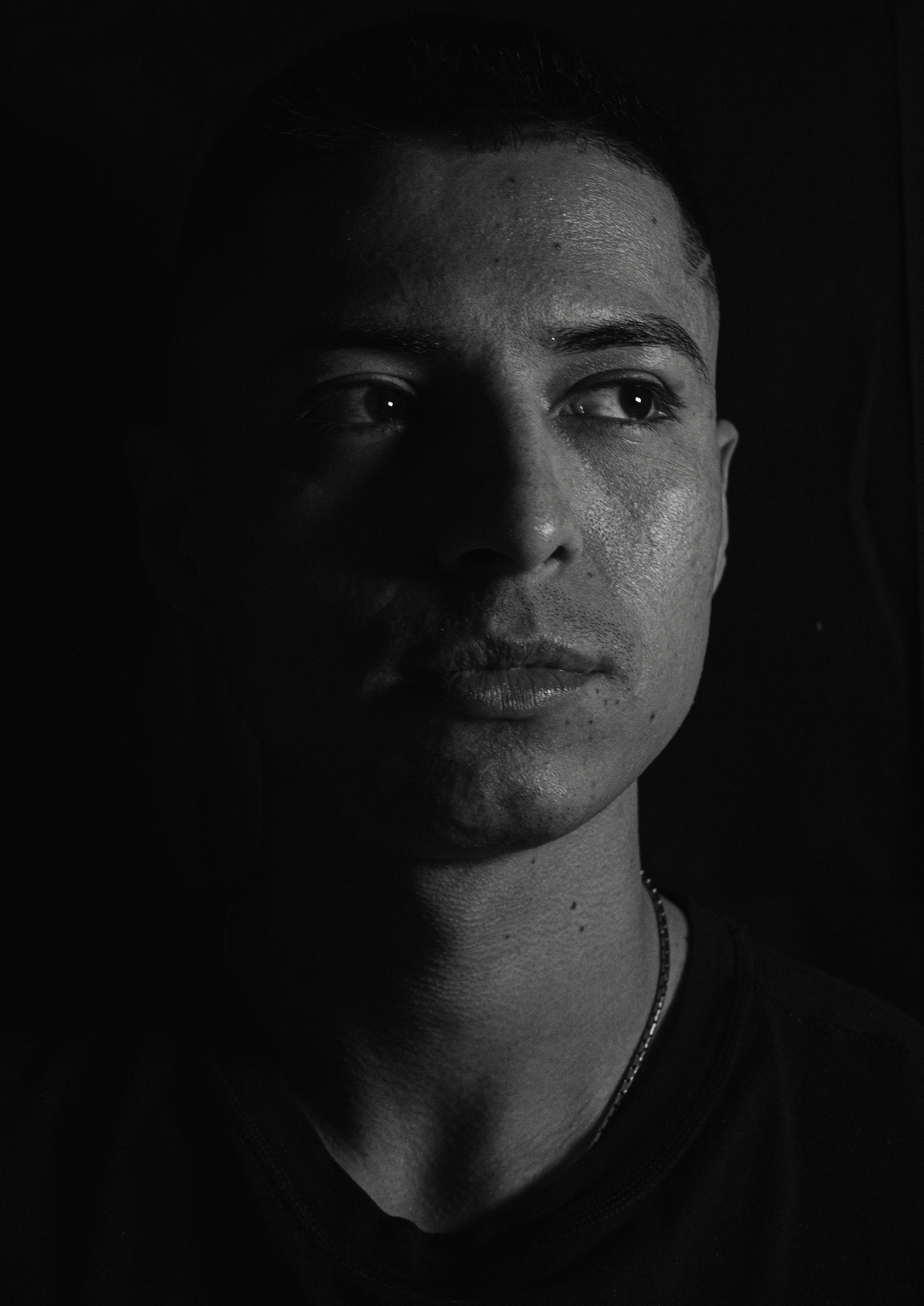 Black and white close-up portrait of a man looking to the side with half of his face in shadow.