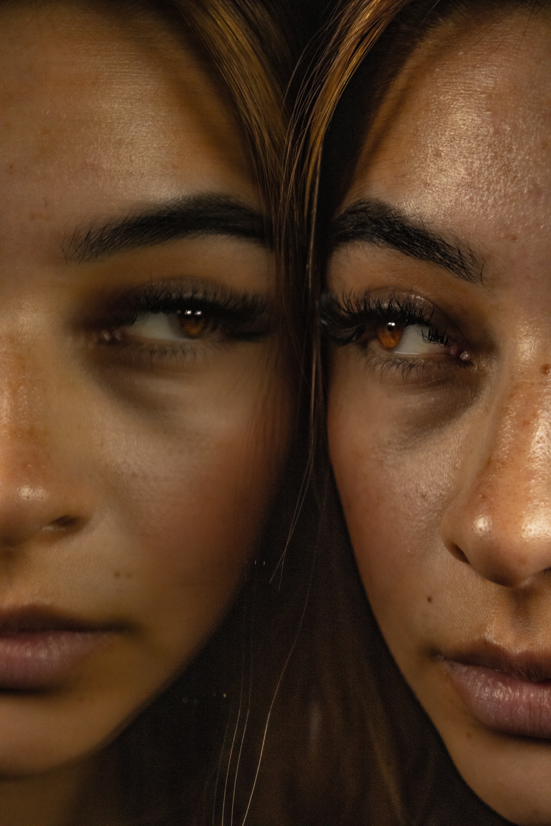 Close-up of a person’s face with brown eyes and freckles reflected in a mirror.