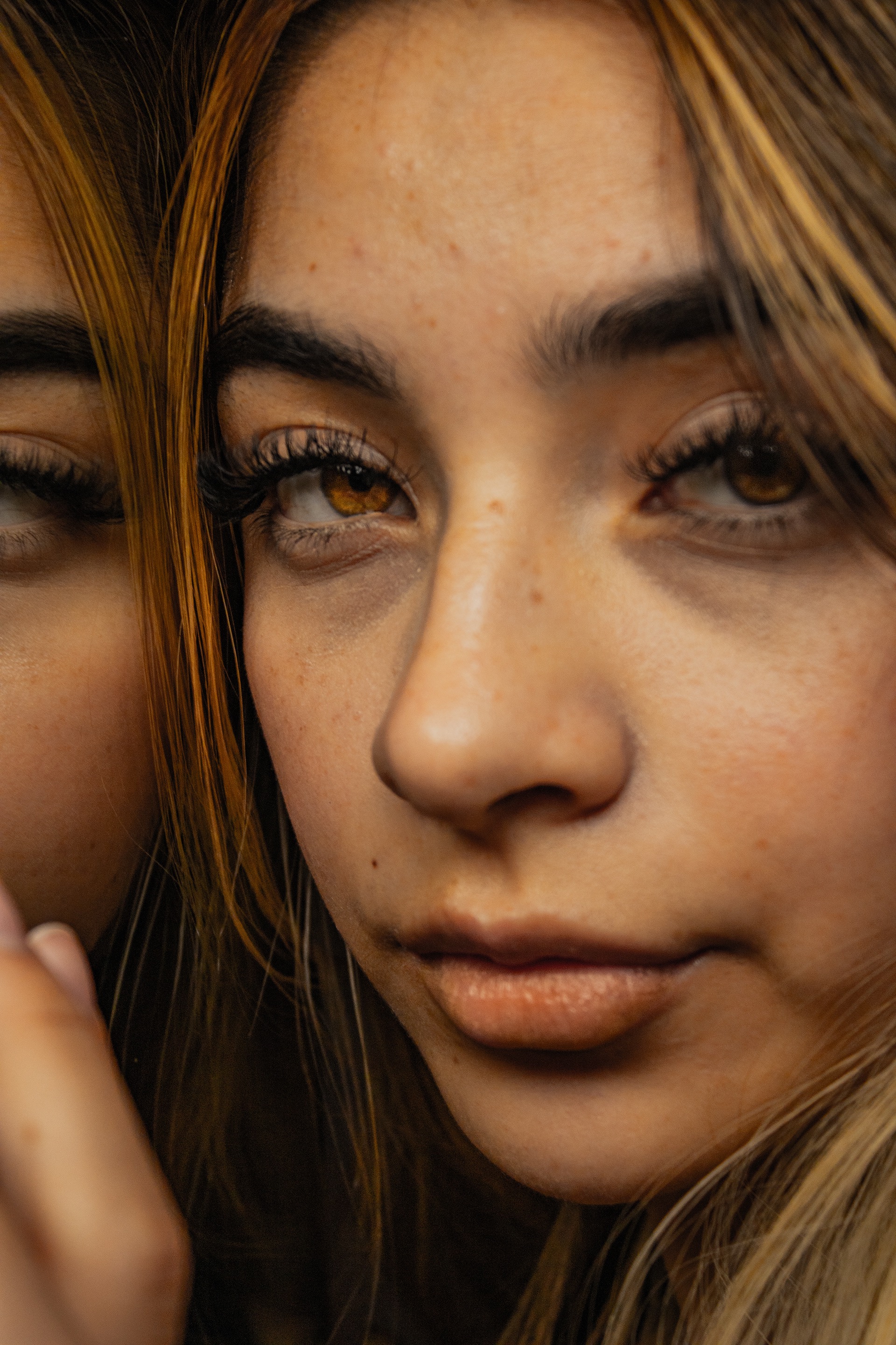 Close-up of a woman's face with light brown eyes, long eyelashes, and light brown hair partially covering her face.