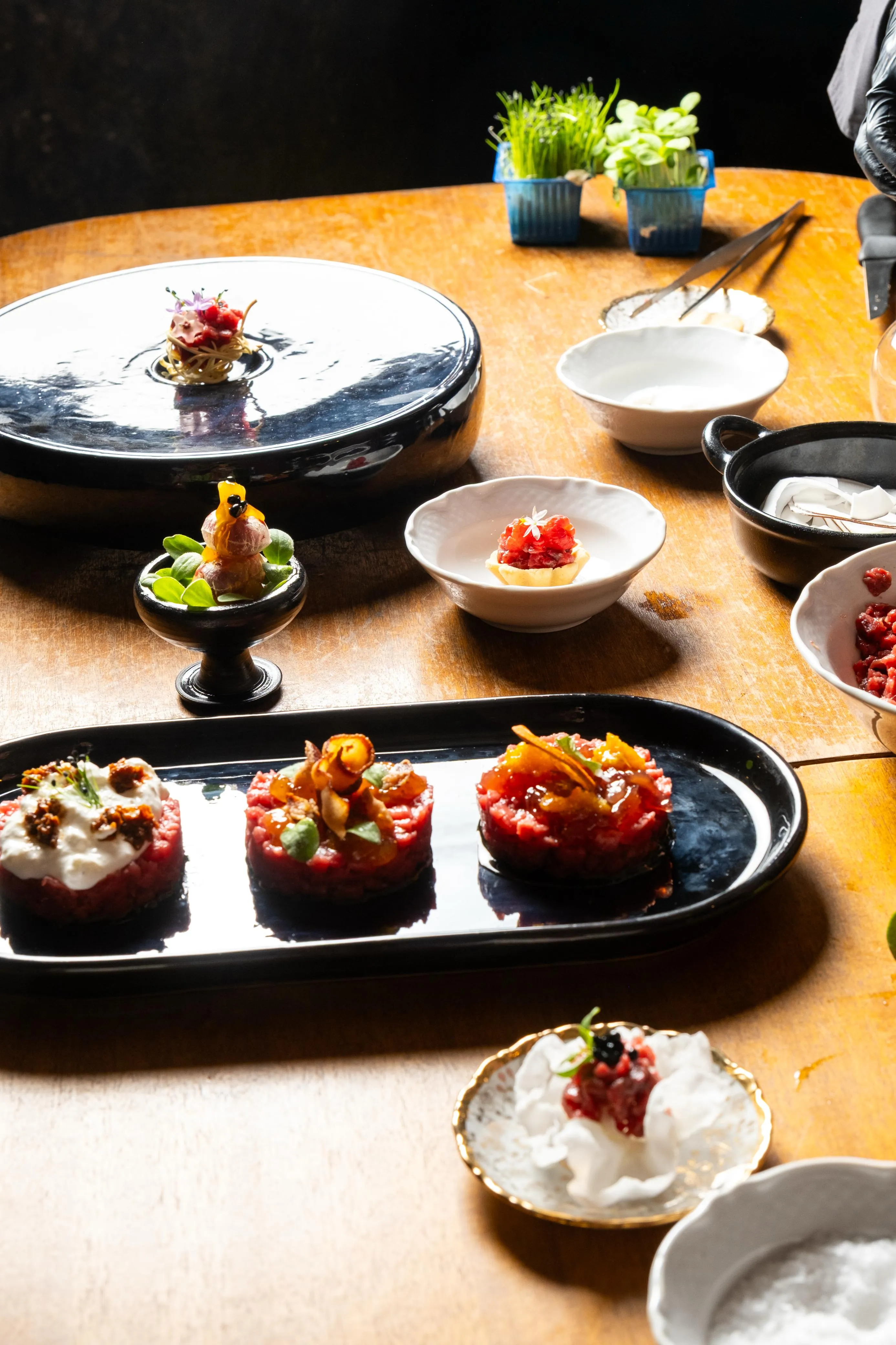 Varie portate di cucina gourmet presentate su piatti neri e bianchi disposti su un tavolo di legno.