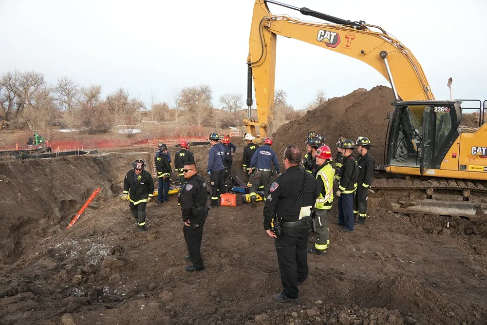 Firefighters and rescue personnel gathered near an excavator during a trench rescue operation