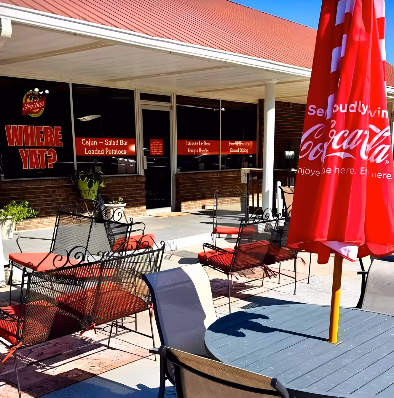 Outdoor seating area with red cushioned chairs and a round table. There is a large red Coca-Cola umbrella.