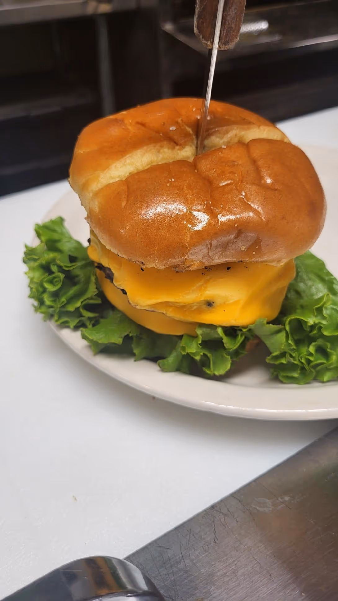 A juicy cheeseburger with melted cheese, fresh lettuce, and a shiny bun is secured with a skewer on a white plate, evoking a hearty, appetizing look.