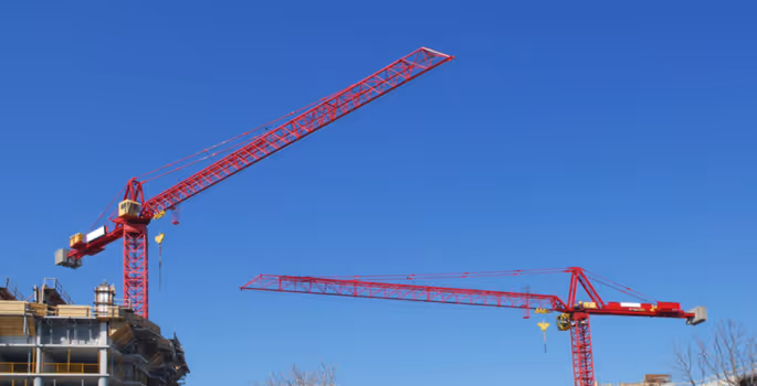 A red crane is standing in front of a building.