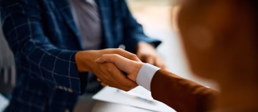 Two people shaking hands while sitting at a table.