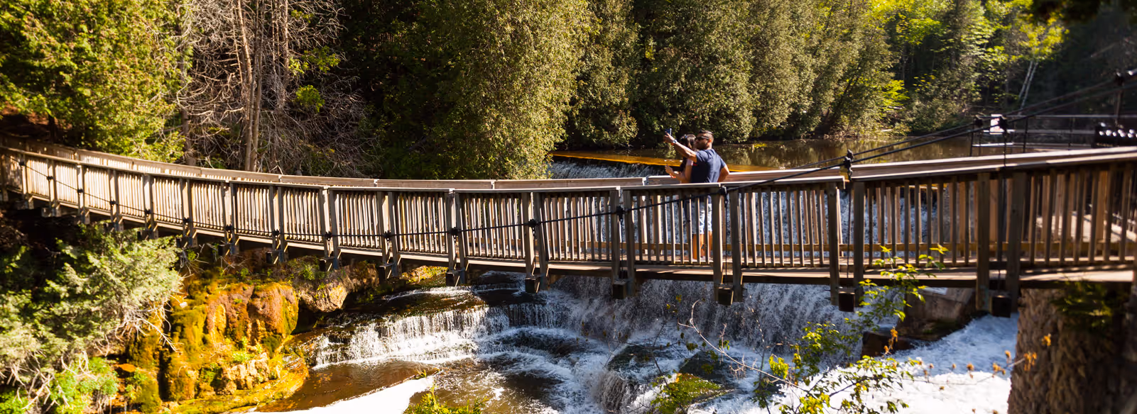 Two people standing on a bridge over a waterfall.