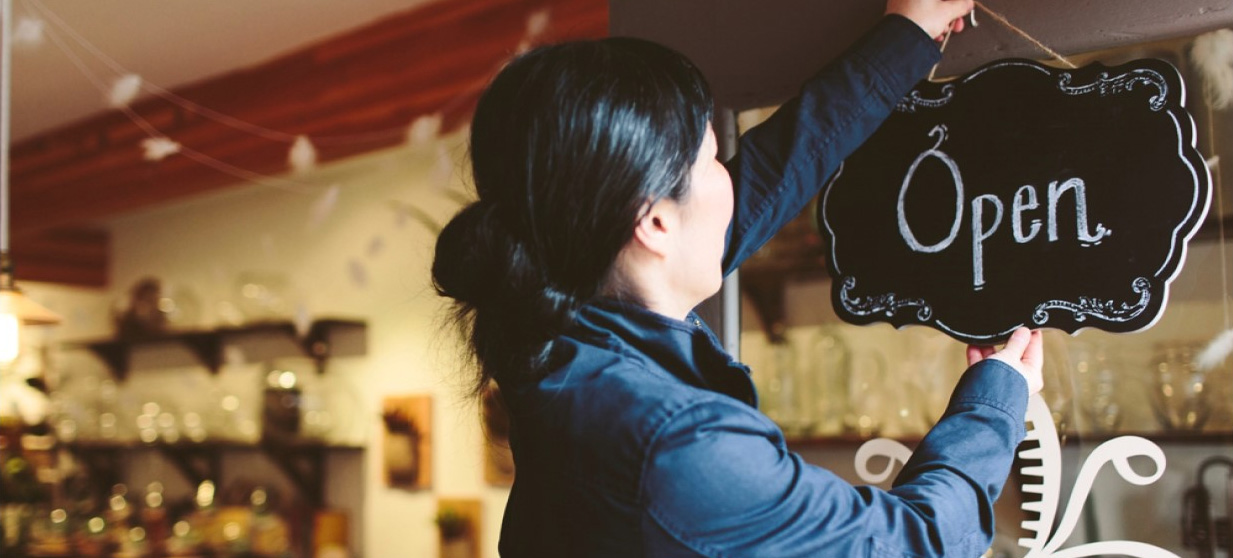 Person hanging a chalkboard sign that reads 'Open' on a shop window.