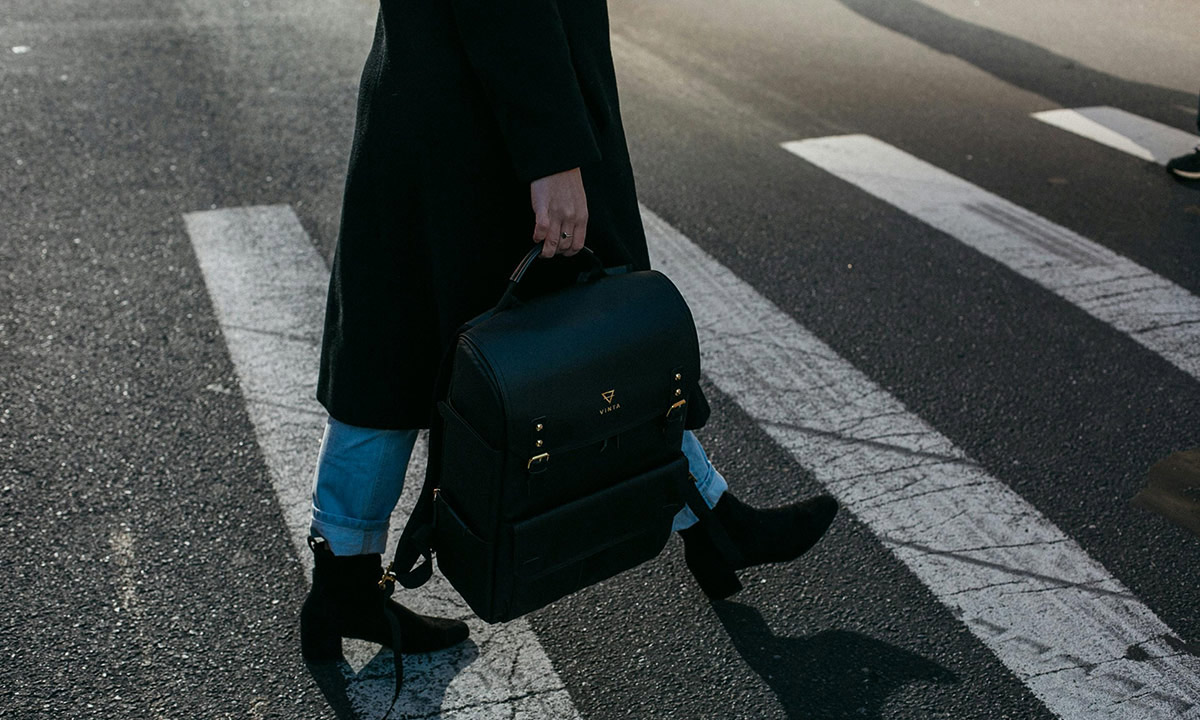 A picture of a person from the waist down as they are walking across a street crosswalk while carrying a briefcase in one hand.