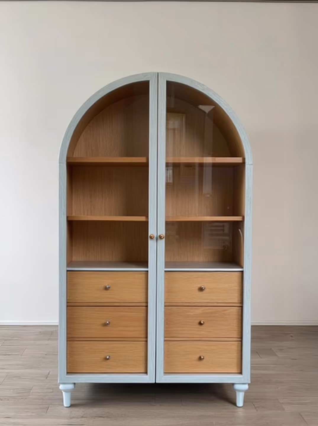 Unique display cabinet by Shohaus featuring an arched silhouette, glass-paneled doors, and a two-tone wood finish‚ perfect for showcasing decor.