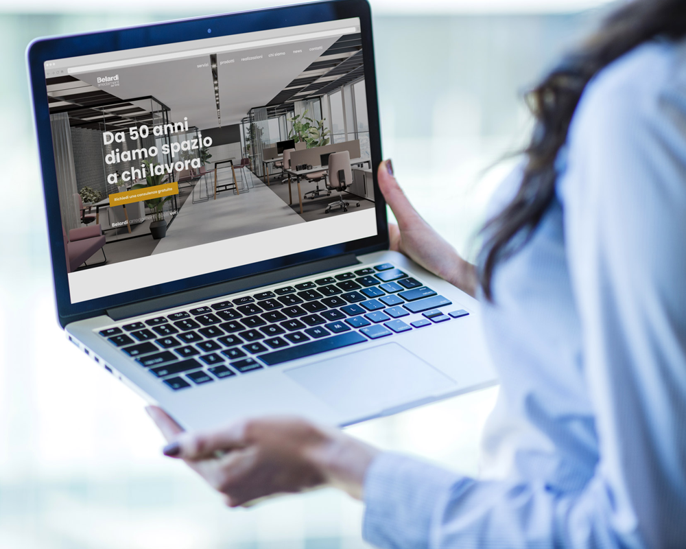 Immagine rappresentativa del cliente Belardi Arredamenti: donna che tiene un computer portatile con la schermata del sito del cliente.