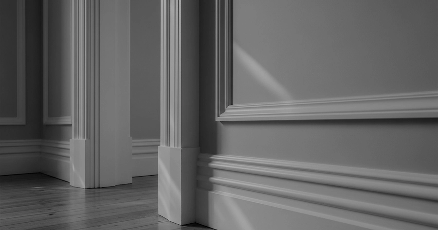 Interior photo showing a corner of a room with decorative moulding, wooden floor, and shadows creating depth in black and white.