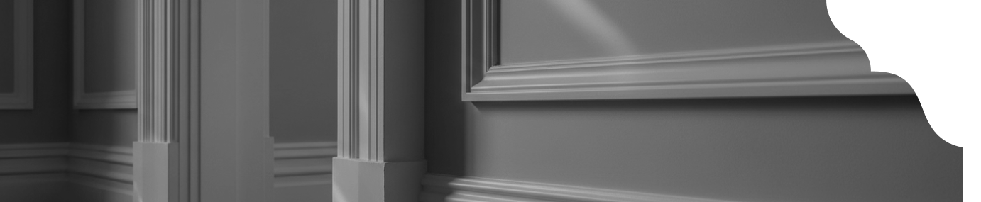 Interior photo showing a corner of a room with decorative moulding, wooden floor, and shadows creating depth in black and white.