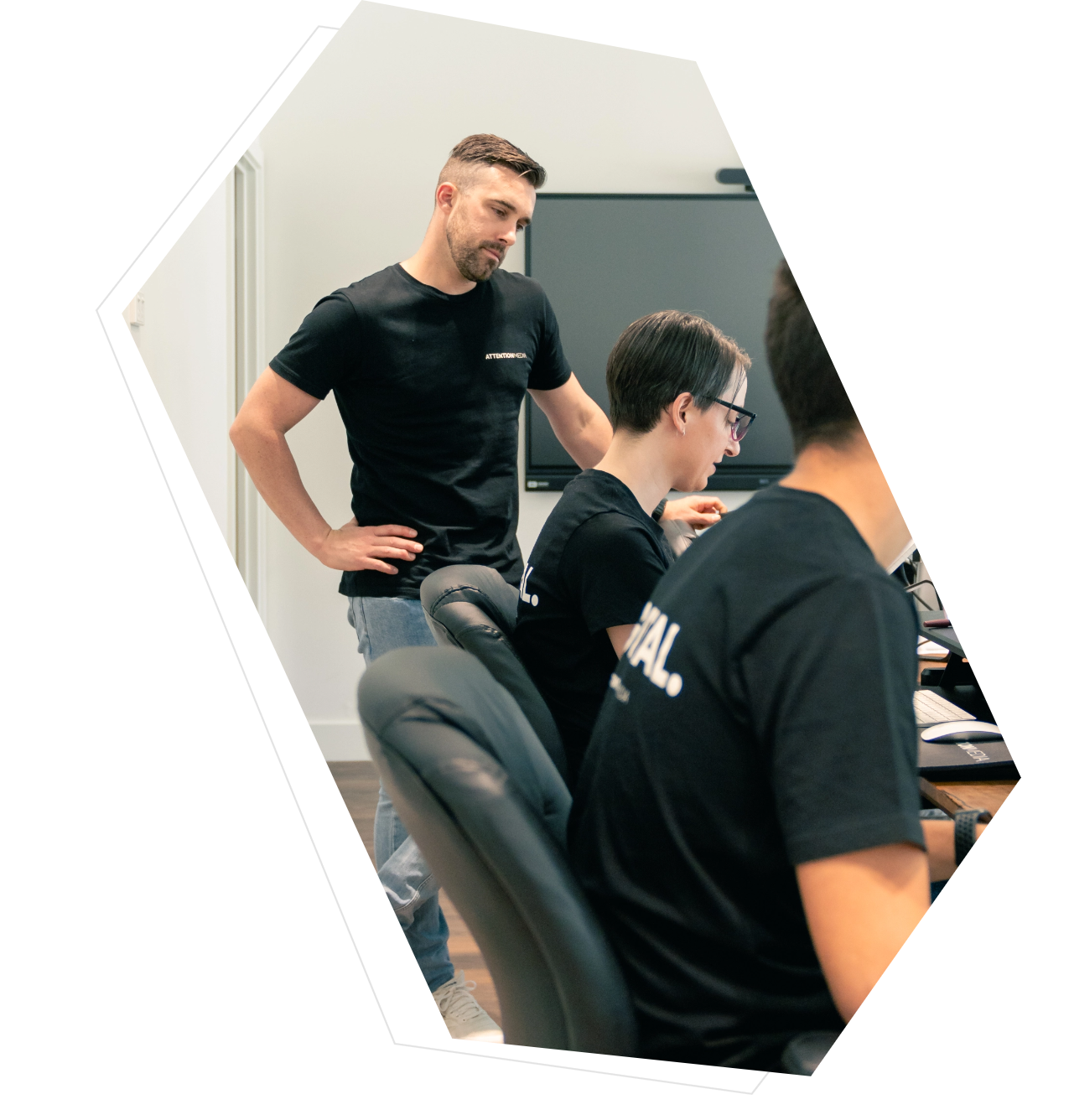 Man standing and observing two seated coworkers working on computers in an office.
