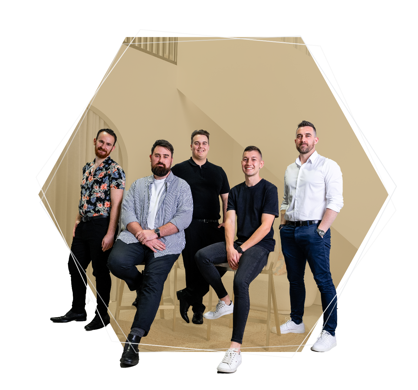 Group of five casually dressed men posing indoors, with two sitting on stools and three standing behind them.