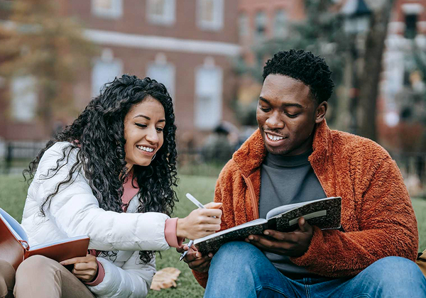 Students smiling, writing in a book together.