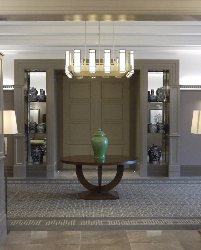 A modern hallway with deep brown tones, featuring a wooden table with a vessel placed on it.