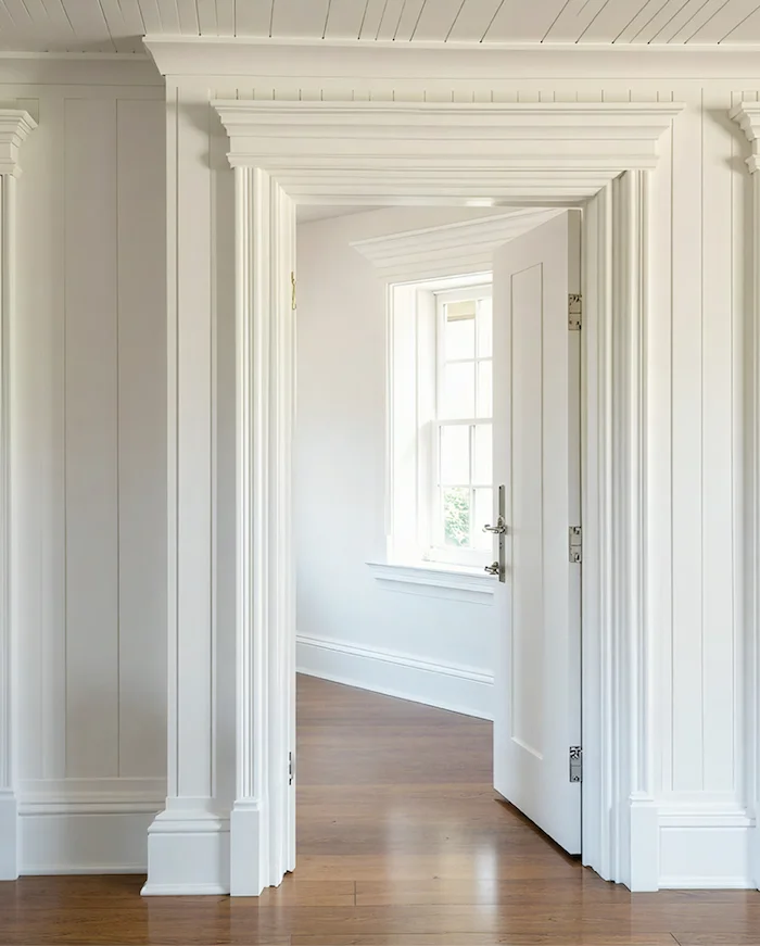Cape Cod style doorway featuring high ceilings, white walls and wooden floorboards.