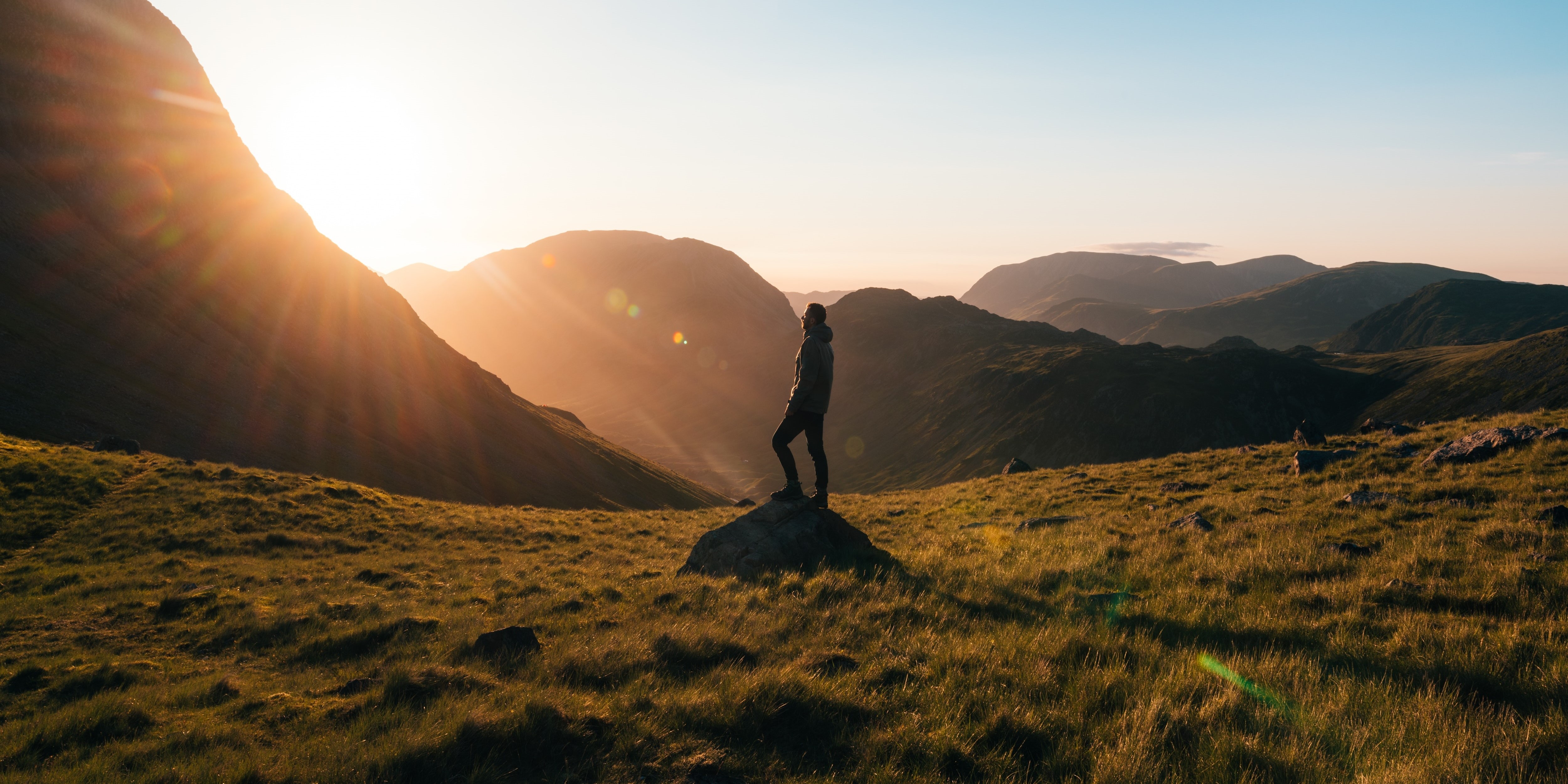Hiker standing on a hilltop at sunrise above a mountain valley