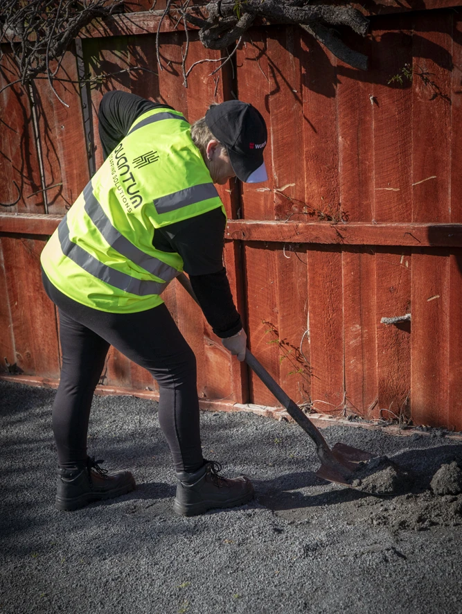 A worker in a Quantum Staffing Solutions branded hi-vis vest shovelling gravel outside.