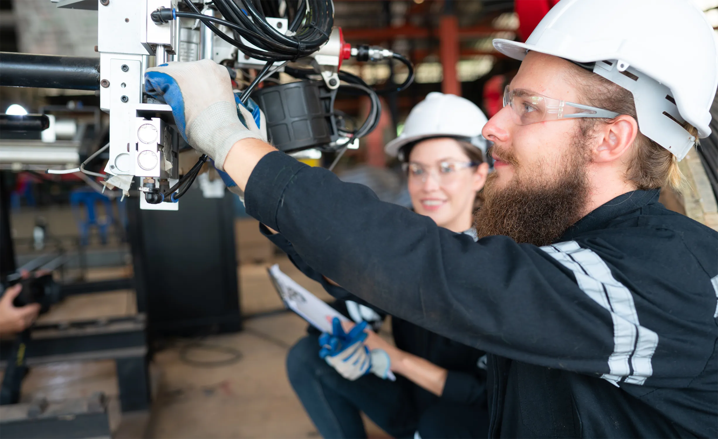 Two workers operating engineering equipment in a workshop.