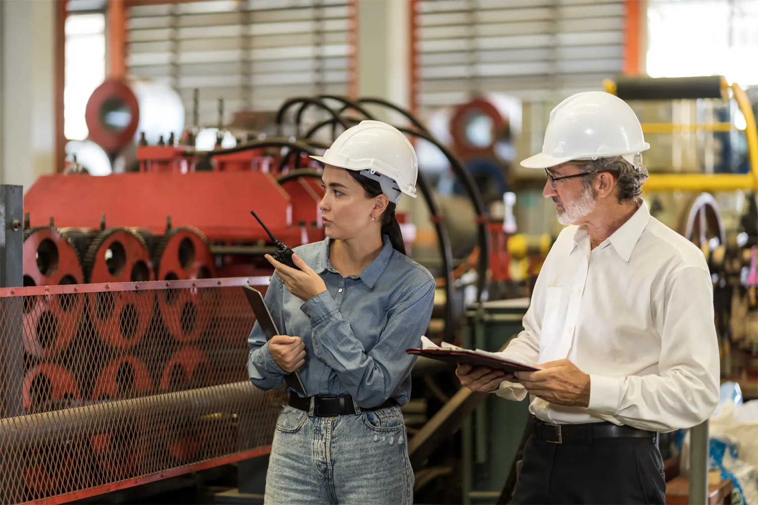 Two workers in a factory setting holding clipboards
