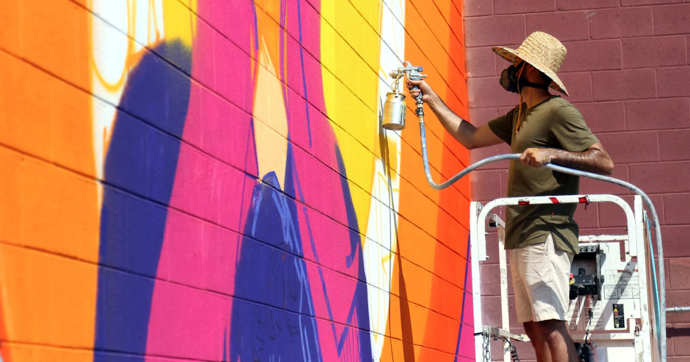 Adam Raiola spray painting a colorful mural on the side of a brick building