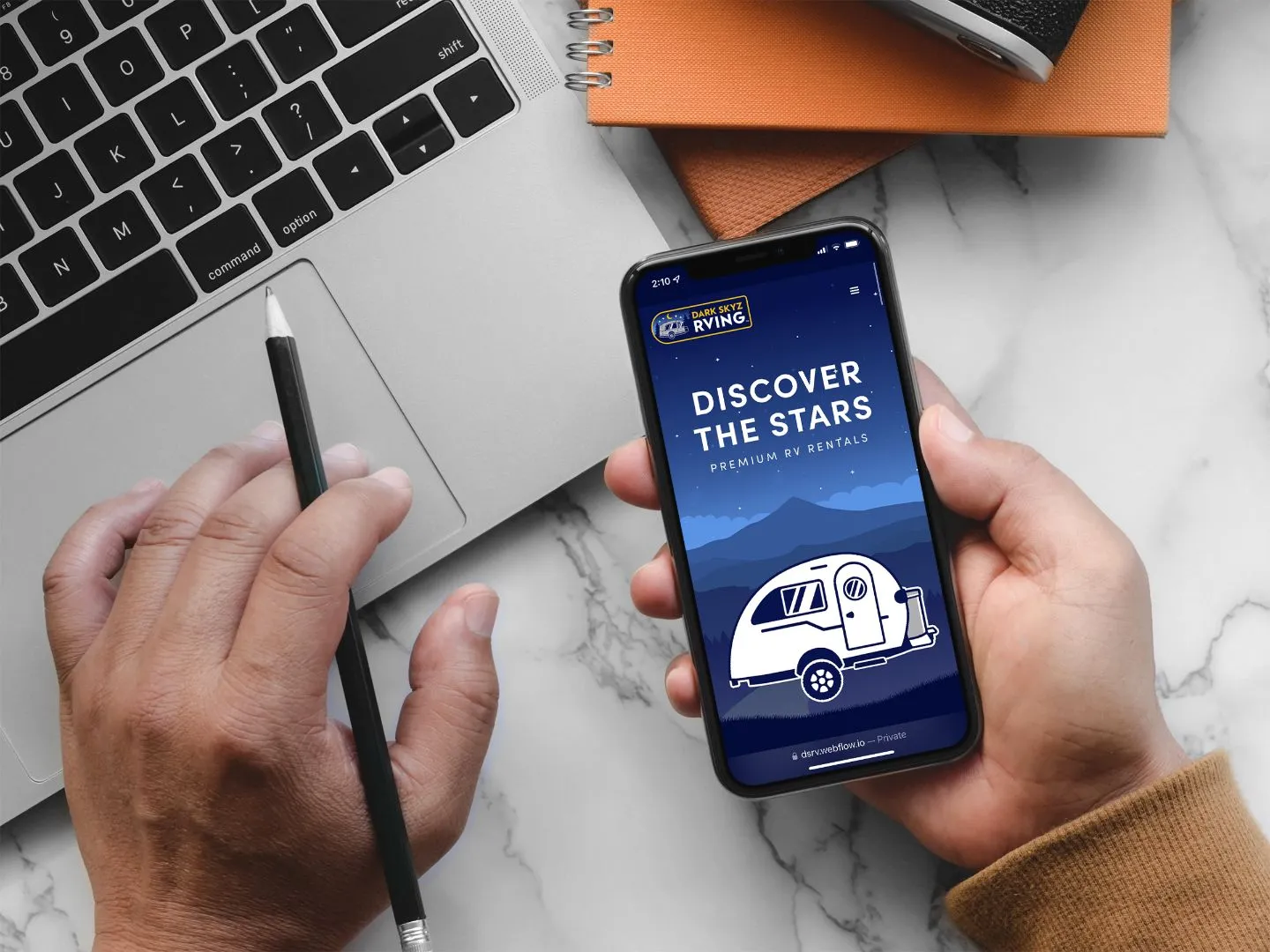 top view of a persons desk with a laptop, notebooks, and hands holding a pencil and a phone