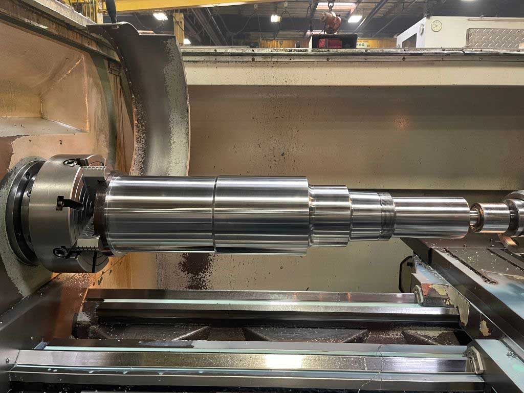 Polished metal cylindrical shaft mounted horizontally in a large industrial lathe machine.