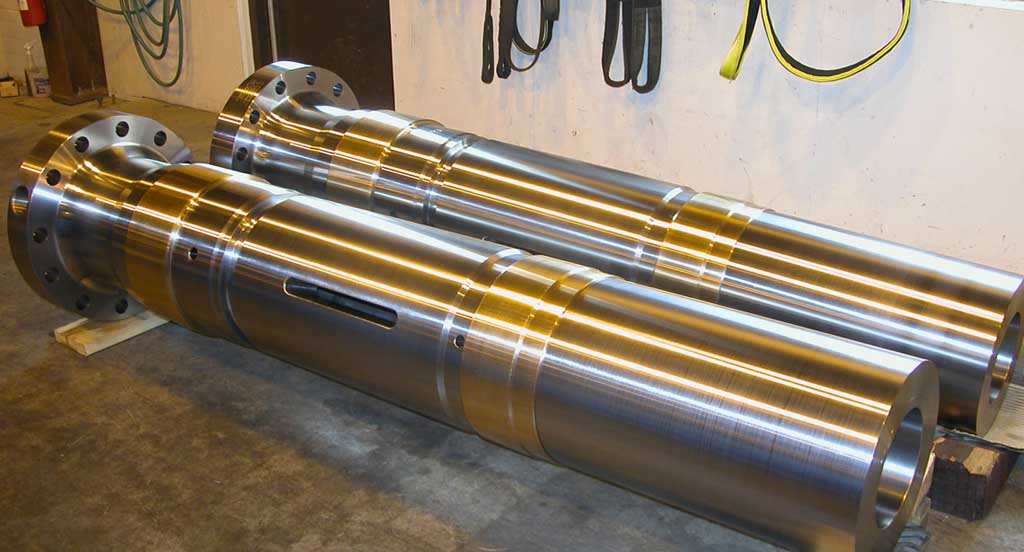 Two large polished metal cylindrical machine parts placed horizontally on a concrete floor in an industrial workshop.