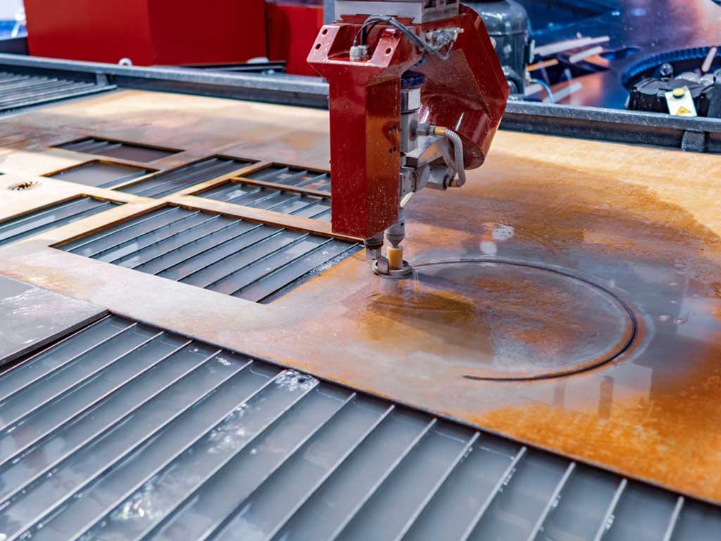 Industrial CNC cutting machine with red head cutting a circular shape into a large rusty metal sheet.