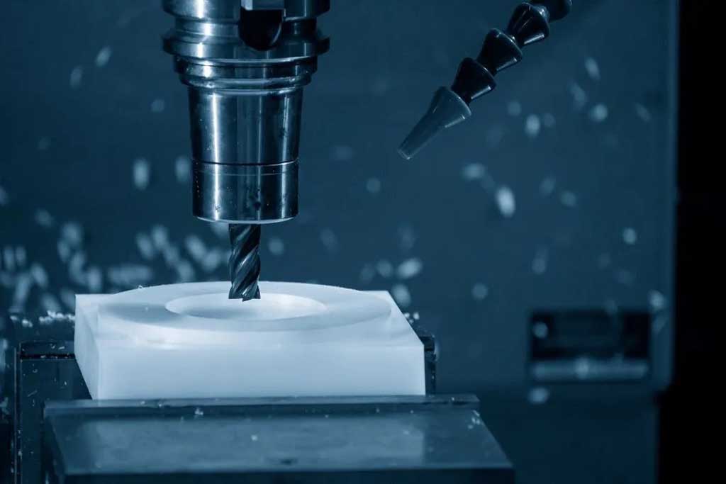Close-up of a CNC milling machine drilling a circular cavity into a white block.