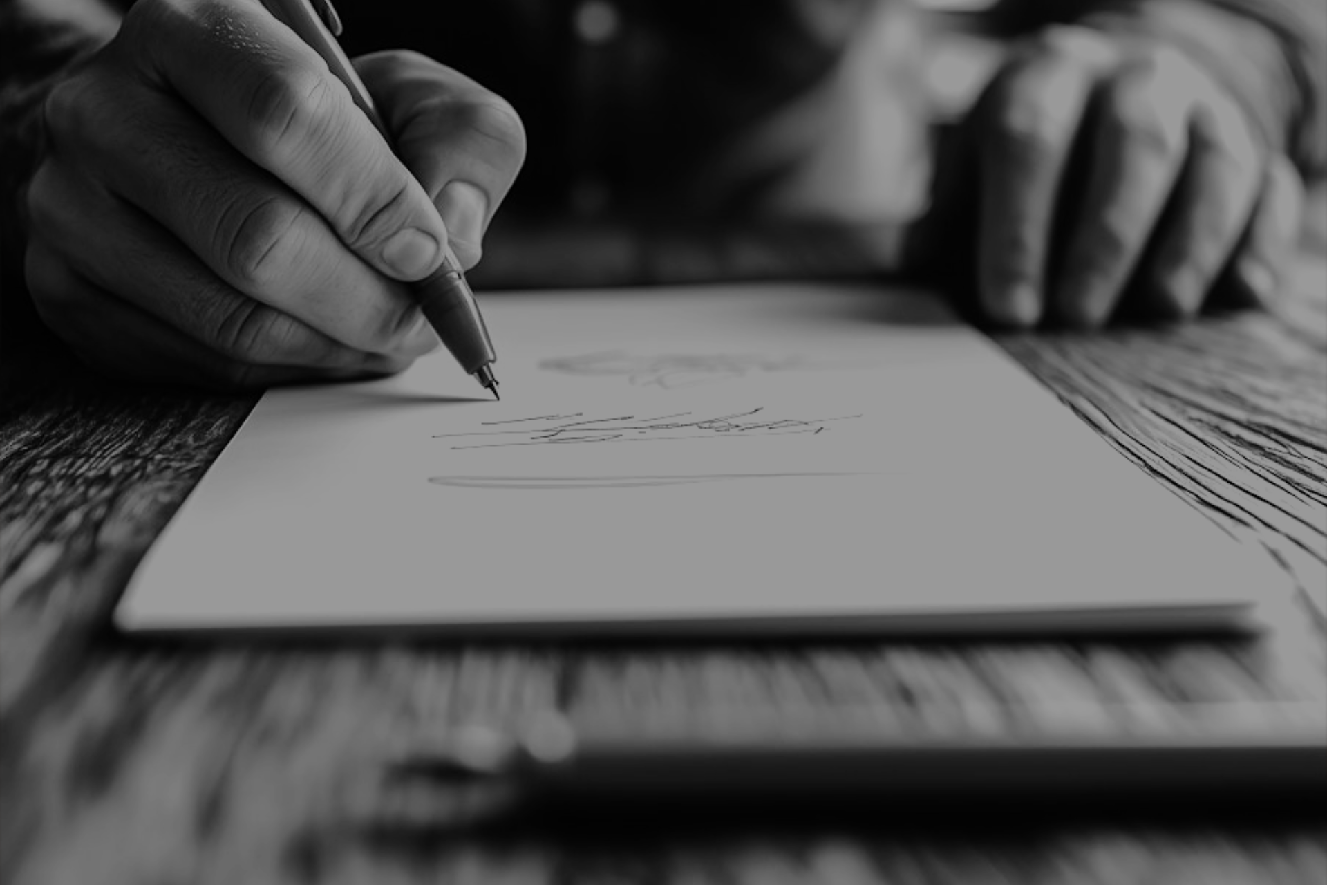 a black and white photo showing a close up of a persons hands, while they write on a sheet of paper