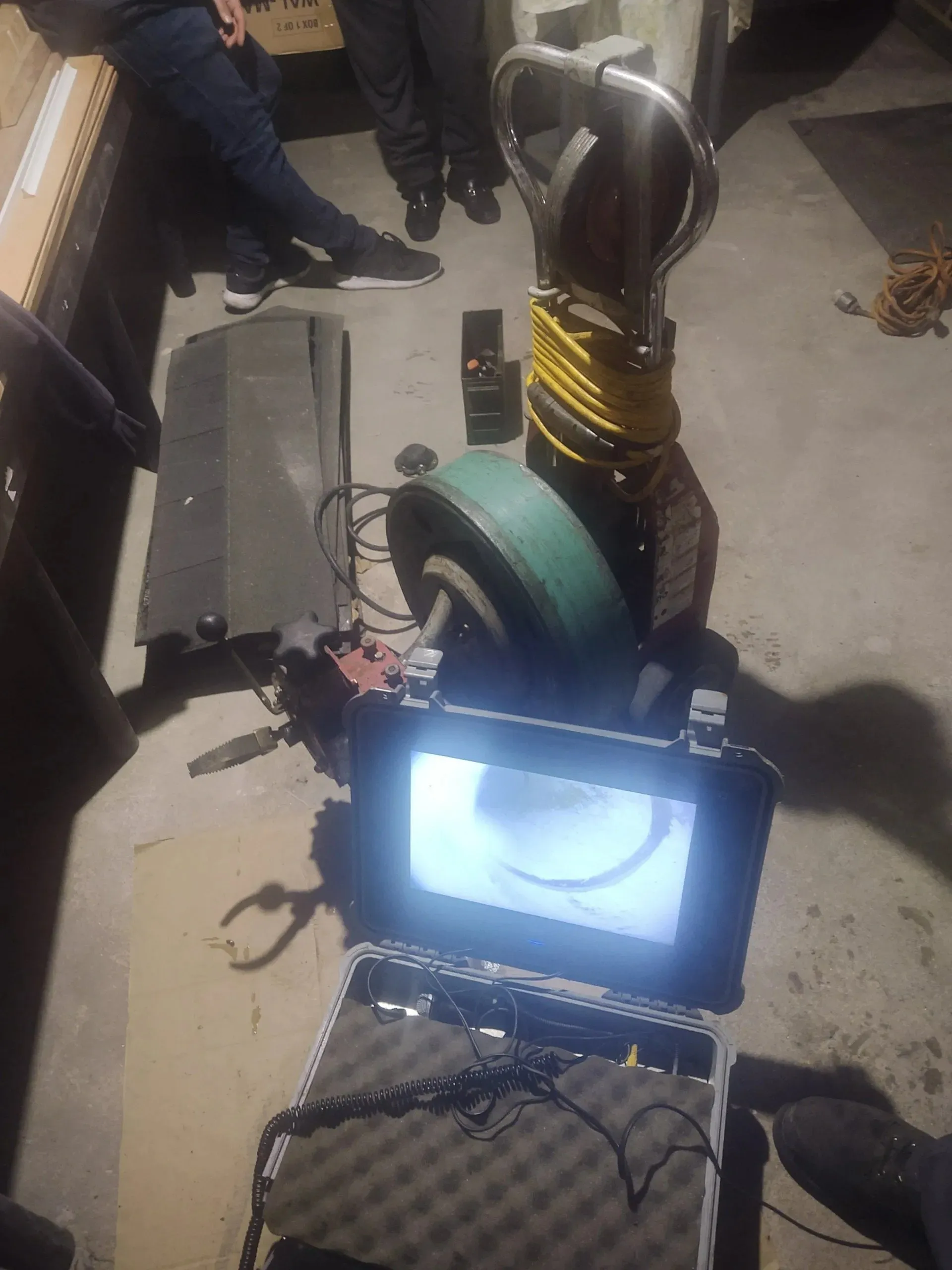 Leak detection equipment with a monitor displaying a pipe interior, green hose reel, and tools on a concrete floor.
