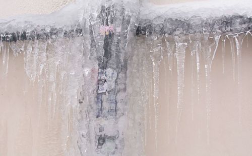 Frozen metal pipe with ice and icicles hanging from it against a beige wall.
