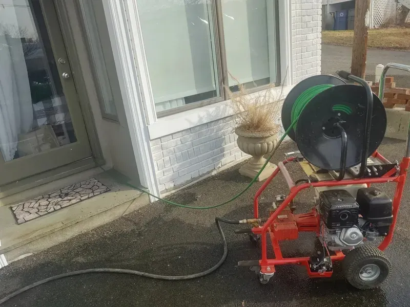 Portable red pressure washer with hose reel on driveway near a white brick house entrance.