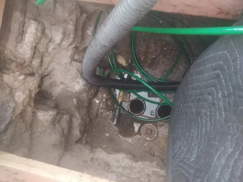 Close-up of a muddy underground utility box with exposed pipes and green cables inside.