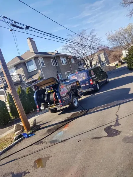 Two dark-colored work vans parked on a residential street near houses and utility poles on a clear day.
