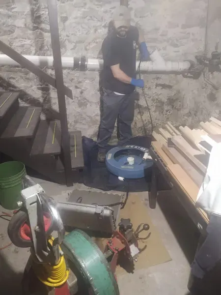 Person wearing blue gloves operating equipment in a basement with stone walls and wooden stairs.