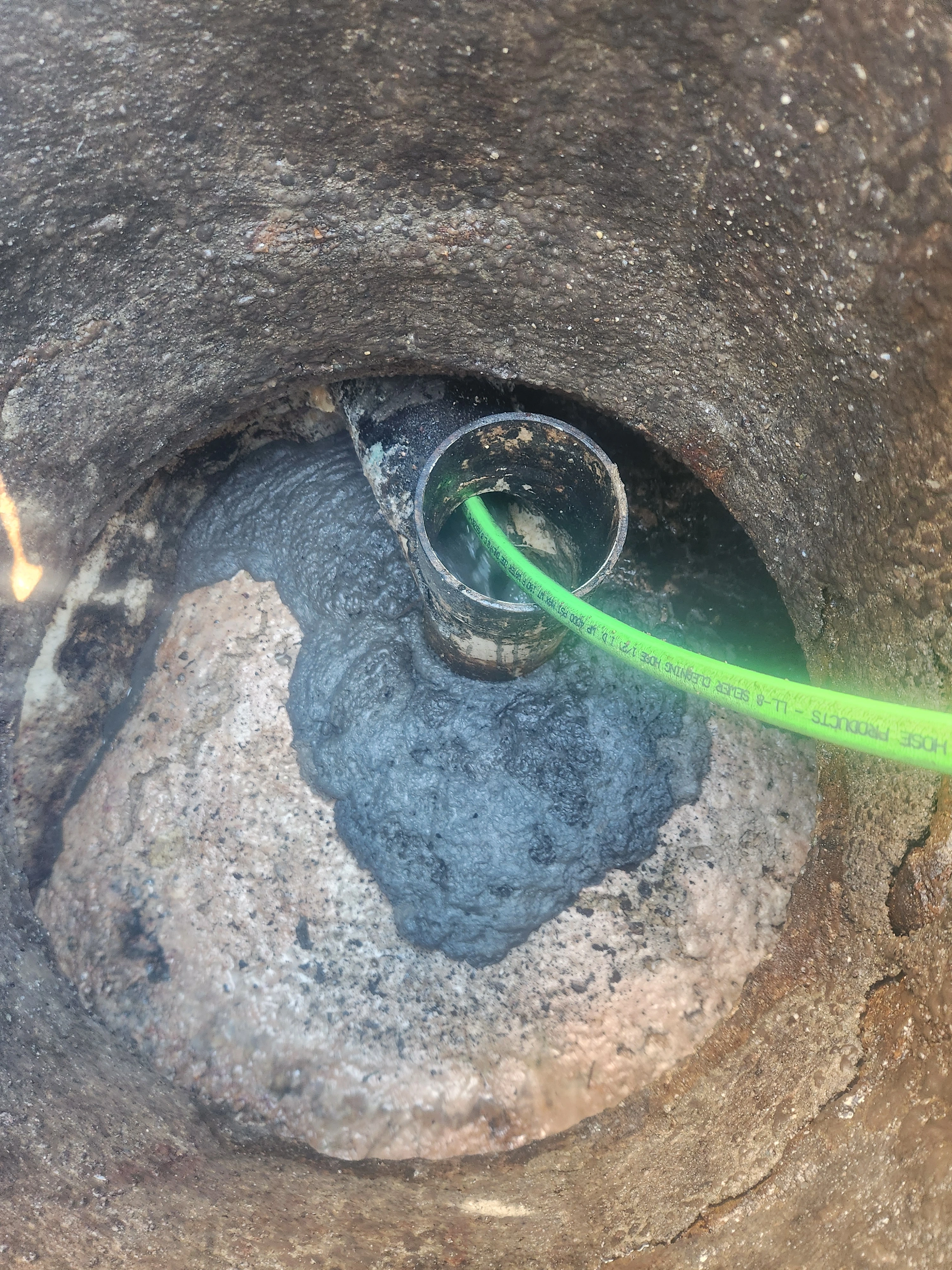 Cleanout access with green hose inserted and fresh pipe lining material visible.