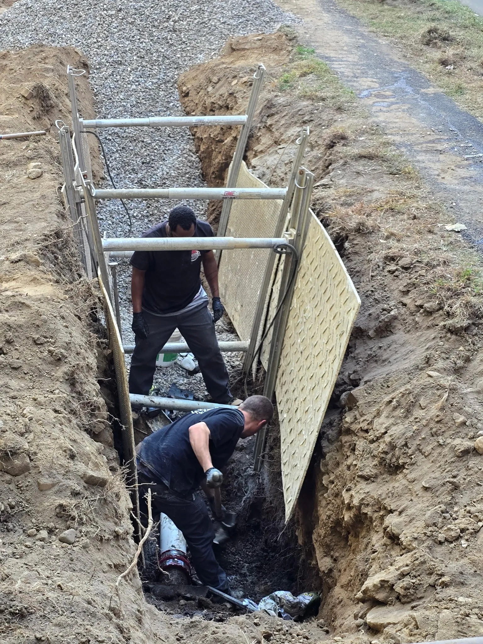 Technicians working inside a shored trench to repair an underground pipe.