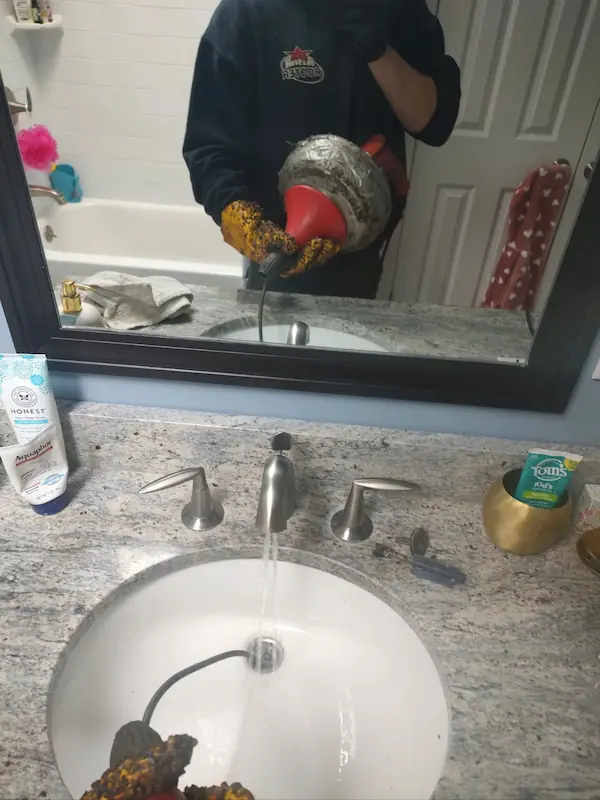 Plumber using drain auger to clear clogged bathroom sink in Norwalk CT