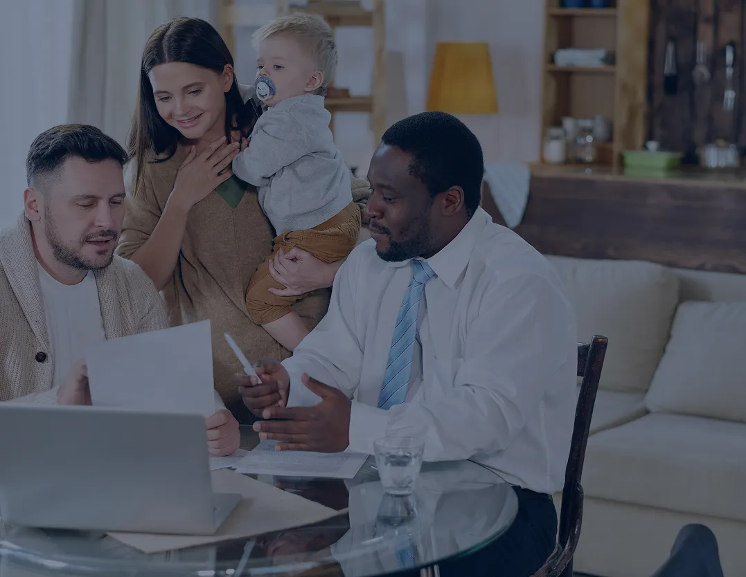 A couple with a baby discussing documents with a professional man in a white shirt and tie at a glass table.