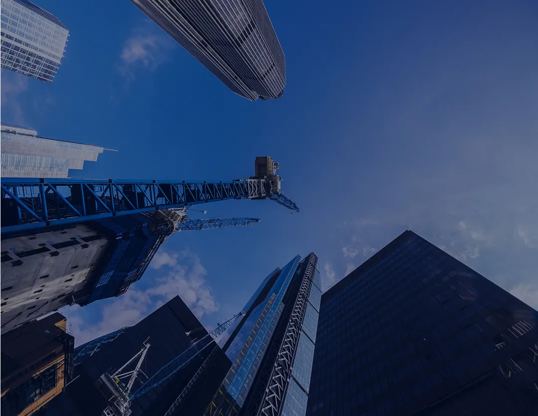 Upward view of multiple modern skyscrapers and construction cranes against a clear blue sky.