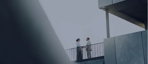 Two business people standing and talking on a balcony outside a modern building.