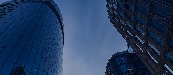 View looking up at modern glass skyscrapers against a clear blue evening sky.