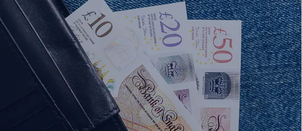 UK £10, £20, and £50 banknotes partially visible inside a black leather wallet on blue fabric.