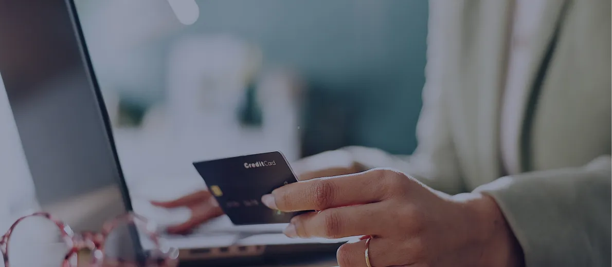 Person holding a credit card near a laptop keyboard, with glasses in the foreground.