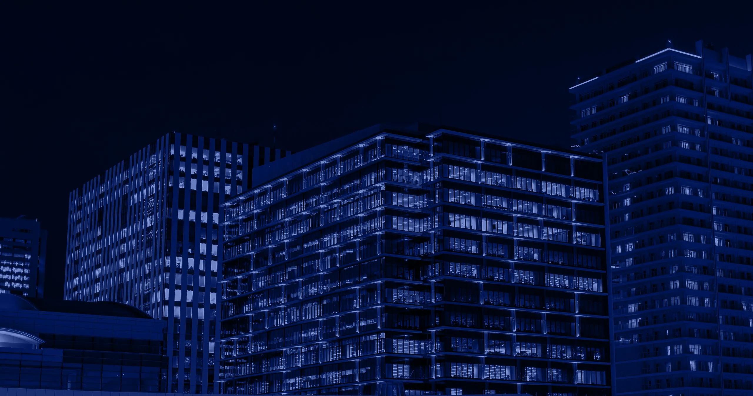 Night view of illuminated modern office buildings with many windows lit up.